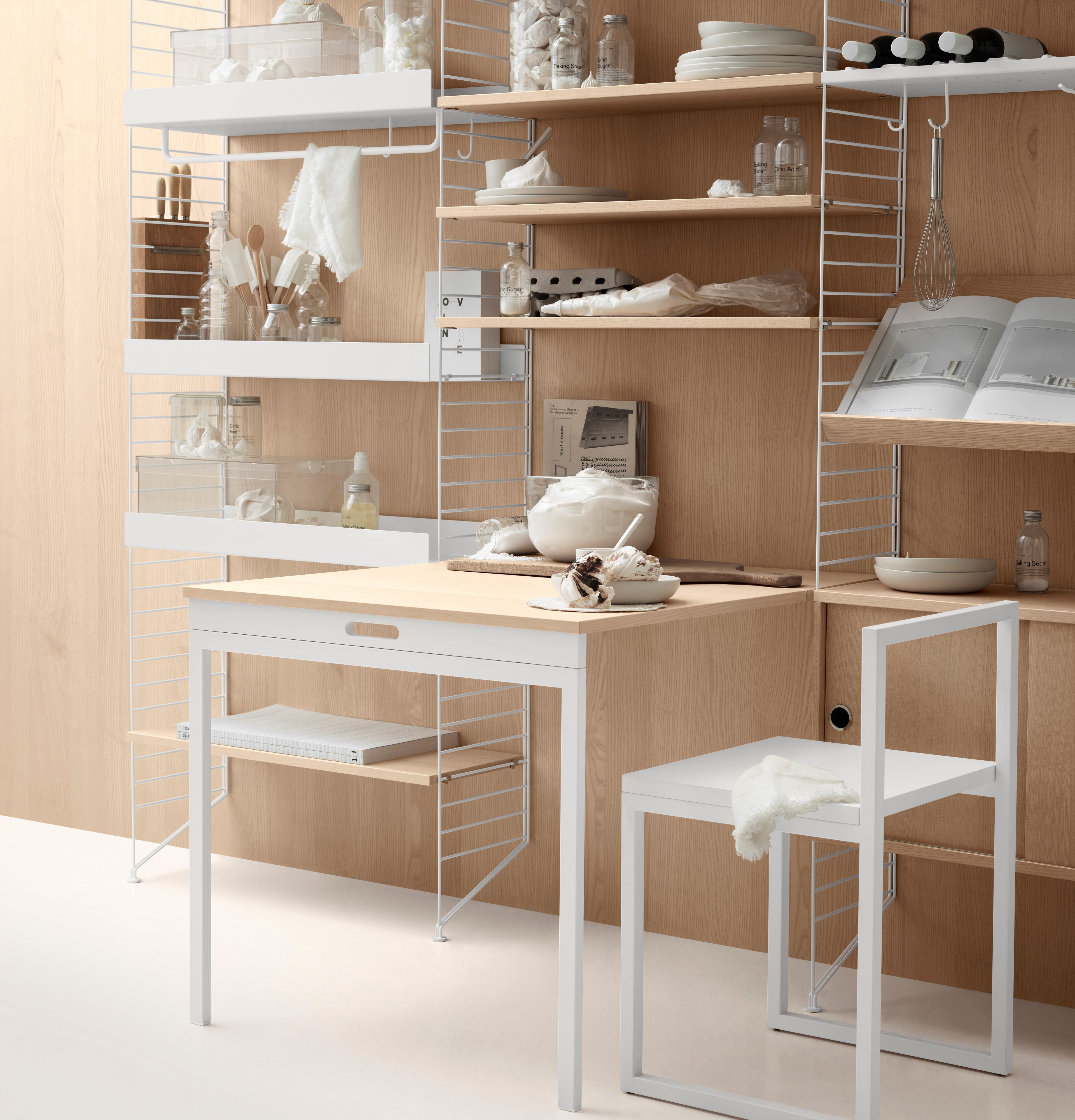 Floor mounted kitchen solution from String. Floor panels in white. Metal shelves high and low, rods, hanger racks, and hooks in white. Shelves, folding table and cabinets with sliding doors in ash.