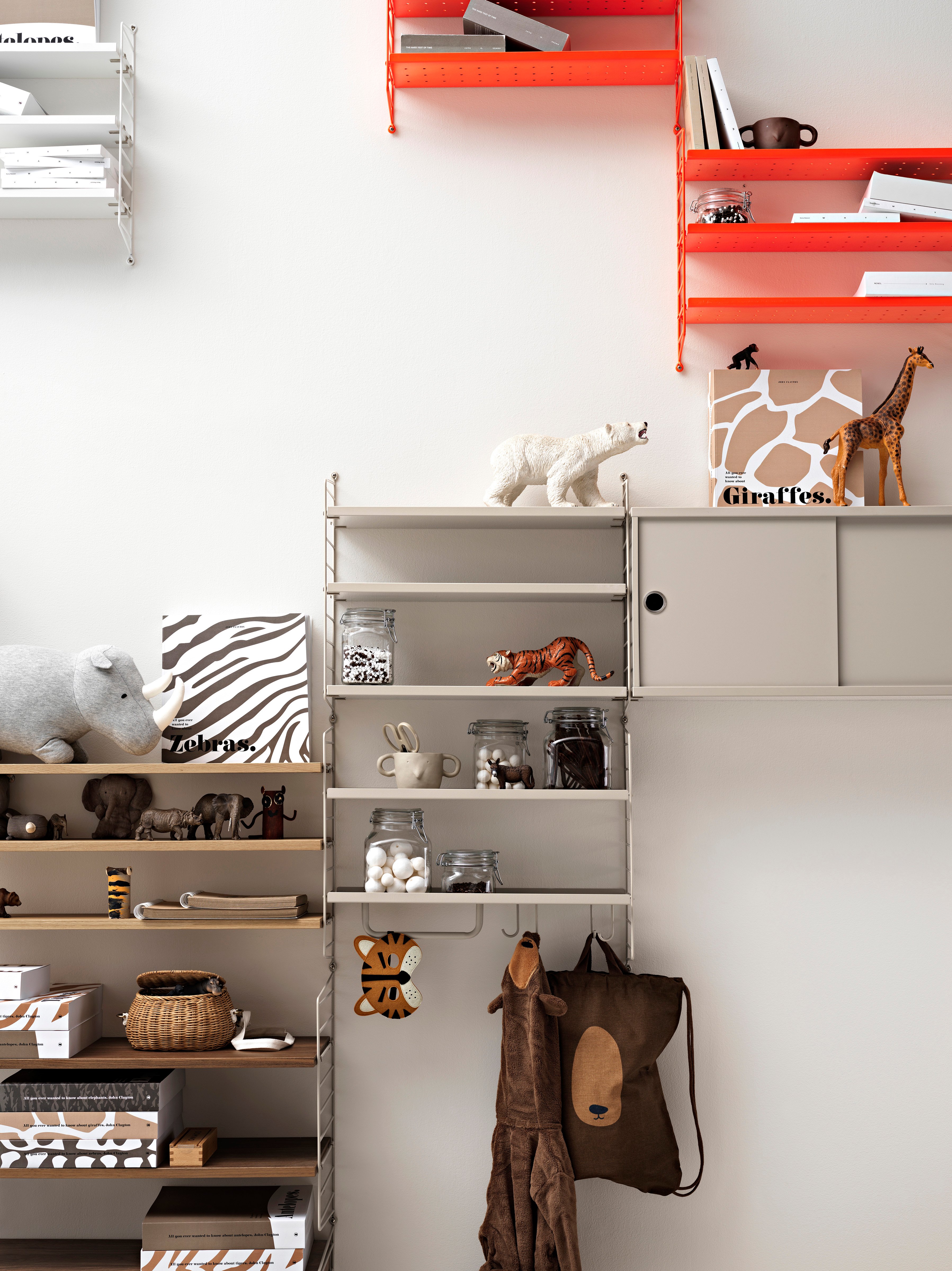 String shelving system för barnrummet. Väggavlar i beige, skåp i beige, metallgyllor med låg kant i beige, hyllor i beige, hyllor i valnöt, stänger i beige och j krokar i beige. String Pocket med perforerade metallhyllor i färgen vit, taupe and neon.