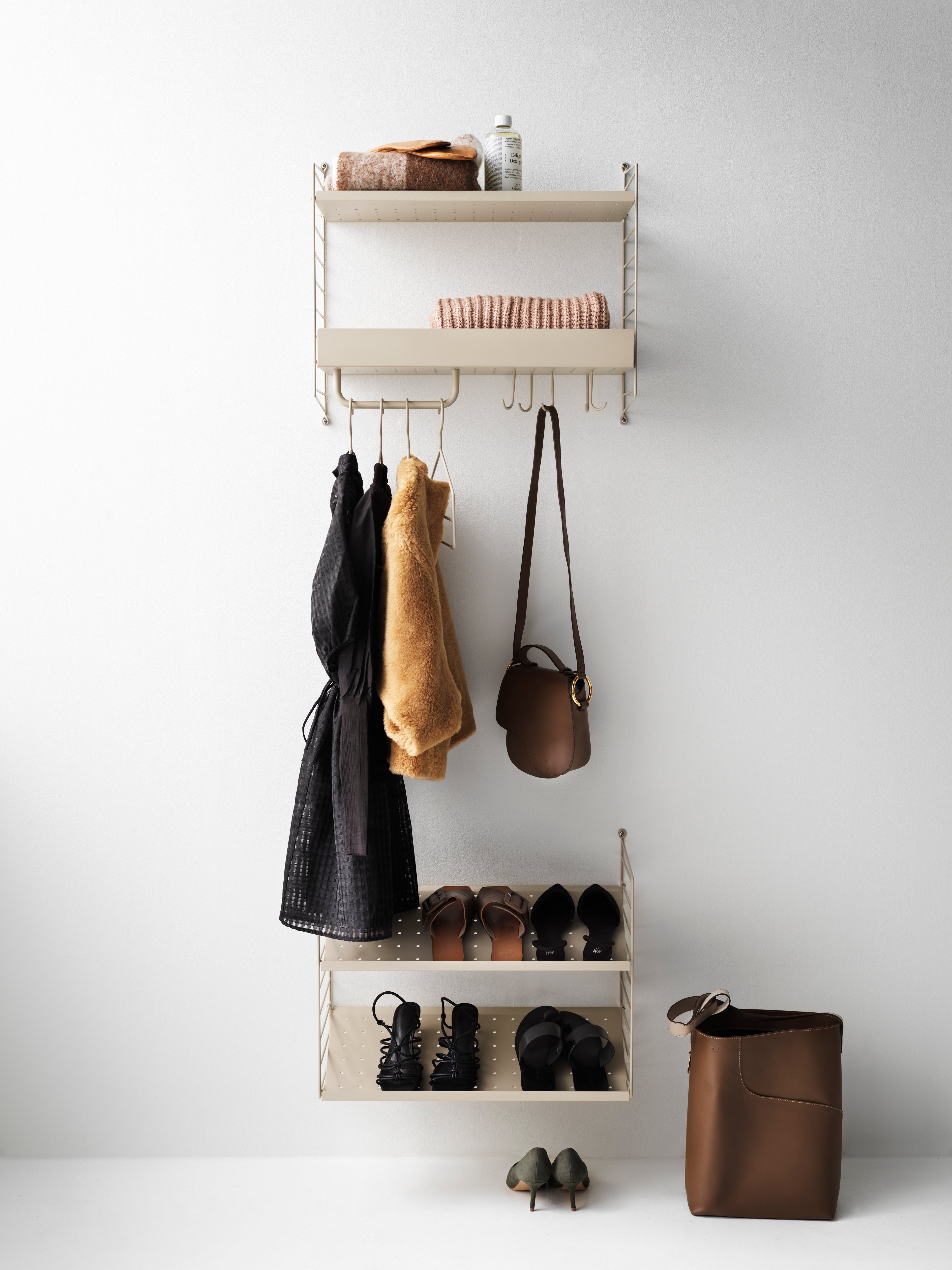 Hallway combination in two sections. The upper section is wall-hung and consists of a metal shelf with low and high edge, hooks, and rods in beige. The lower section is also wall-hung and consists of shoe shelves in beige.