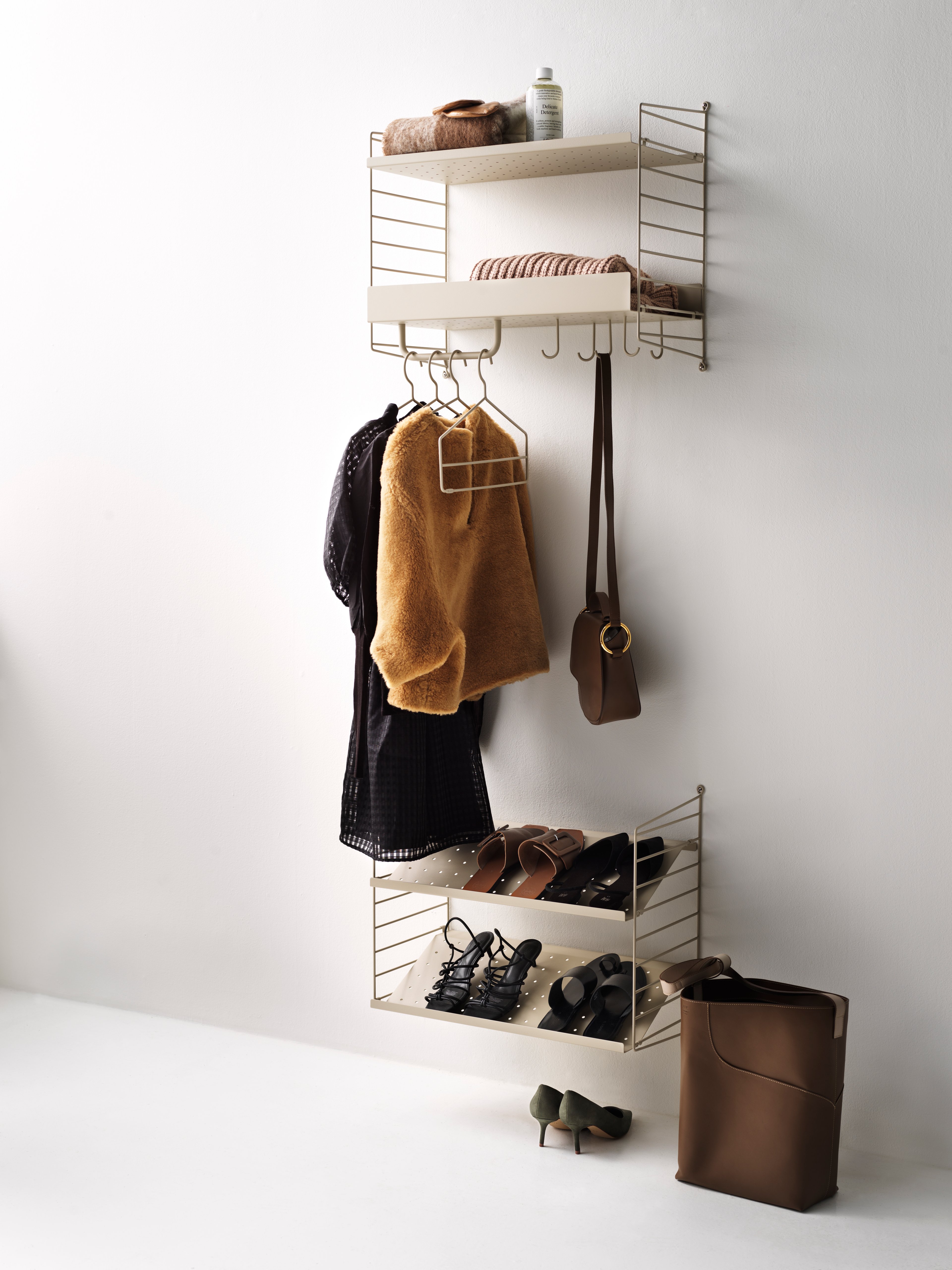 Hallway combination in two sections. The upper section is wall-hung and consists of a metal shelf with low and high edge, hooks, and rods in beige. The lower section is also wall-hung and consists of shoe shelves in beige.