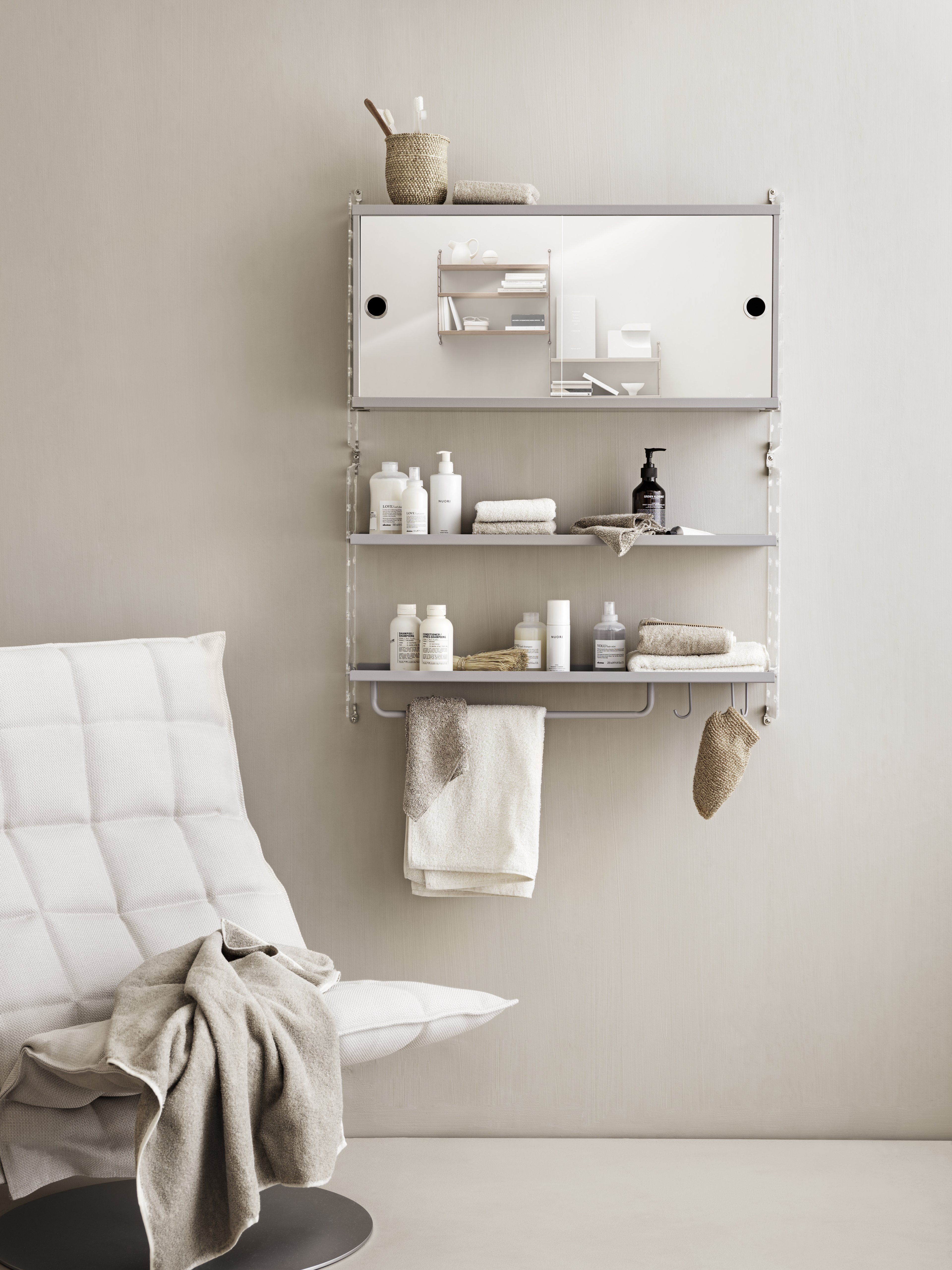 Wall mounted bathroom solution from String. Wall panels in clear perspex, metal shelves with low edge and cabinet with sliding doors, rod and hooks in grey.