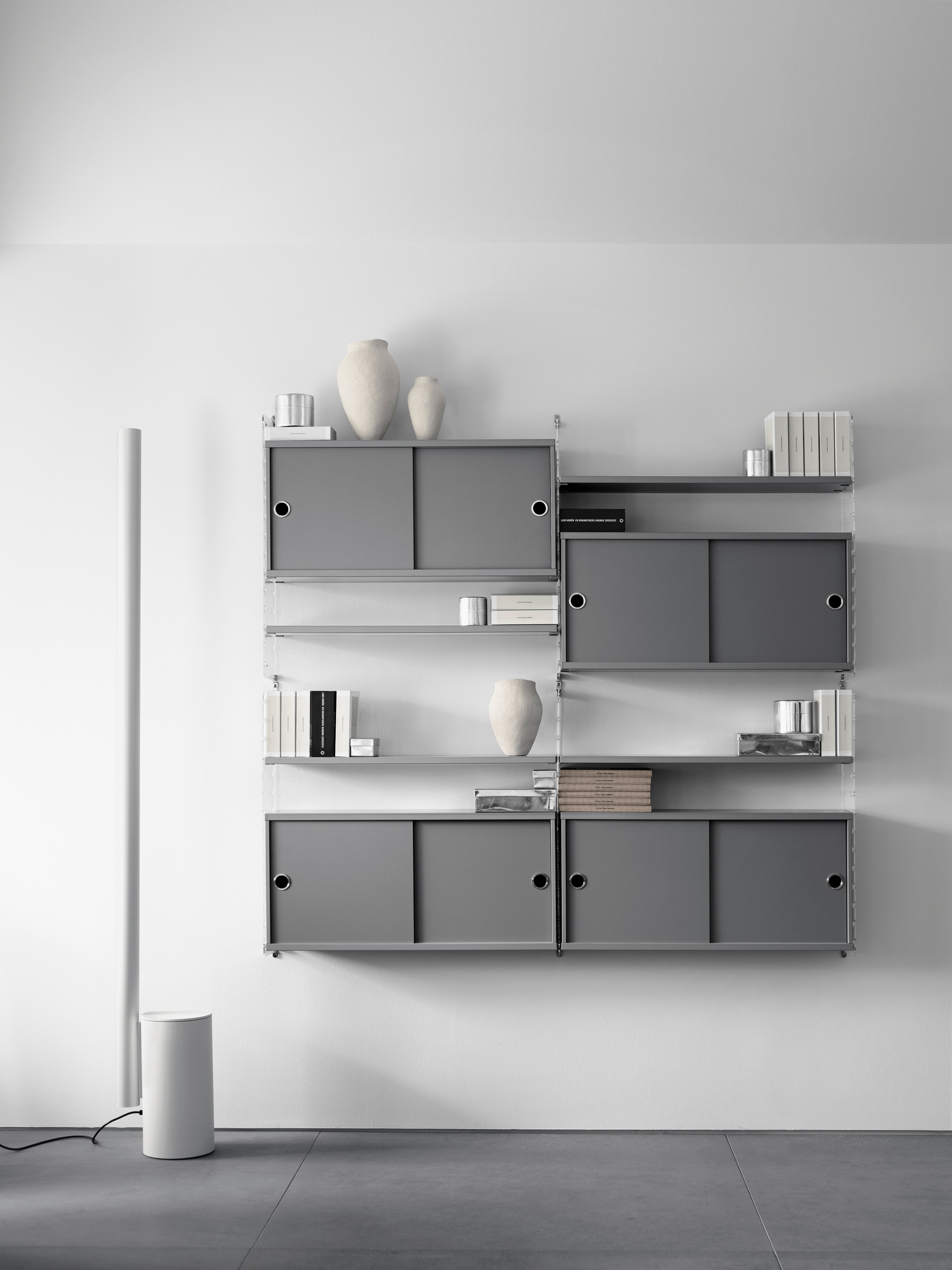 Solución de sala de estar montada en pared de String. Paneles de pared de plexiglás y estantes en gris. Cabinet con puertas correderas en gris.