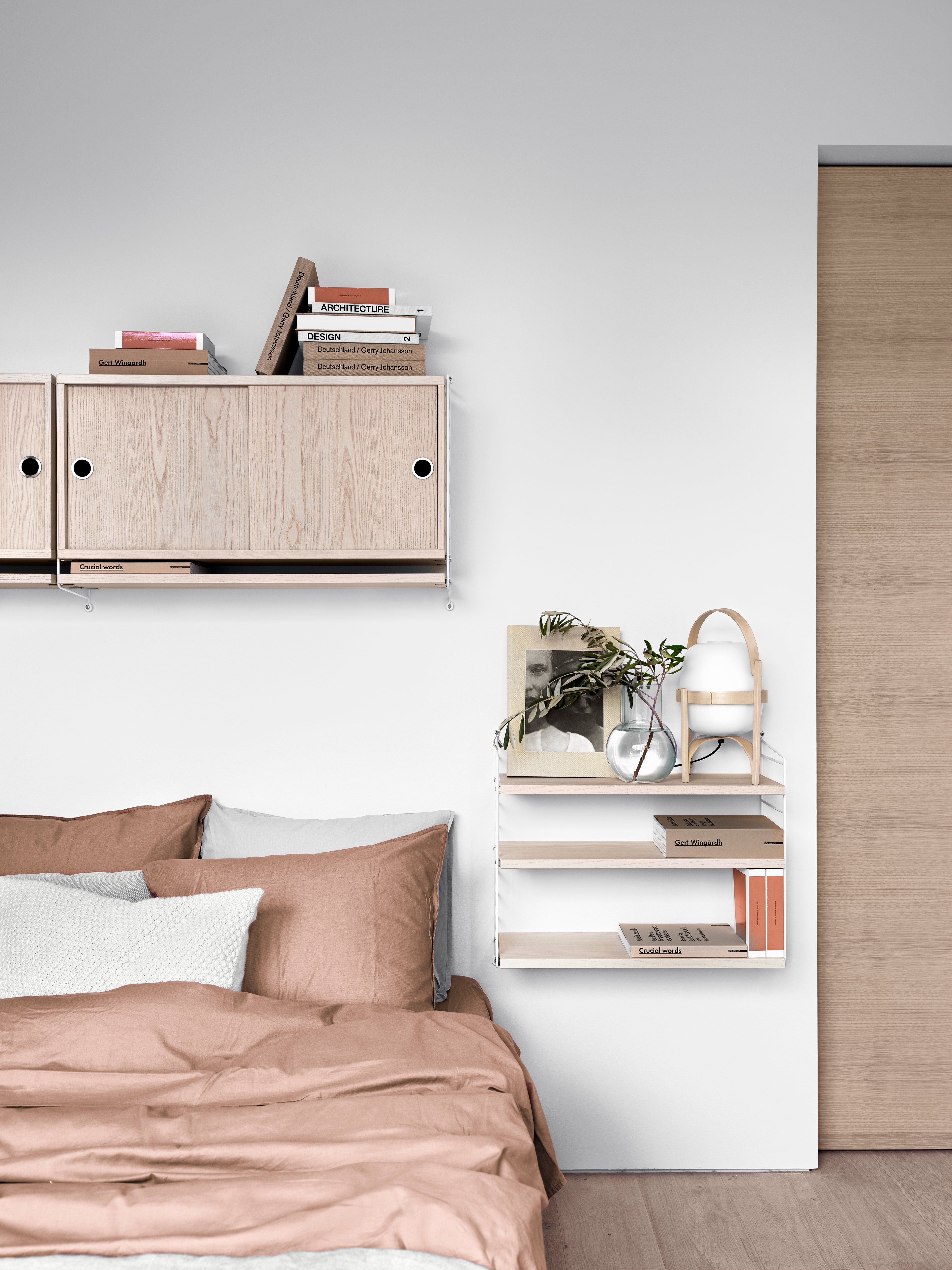 Wall mounted bedroom solution from String. Wall panels in white. Shelves and cabinets with sliding doors in ash.