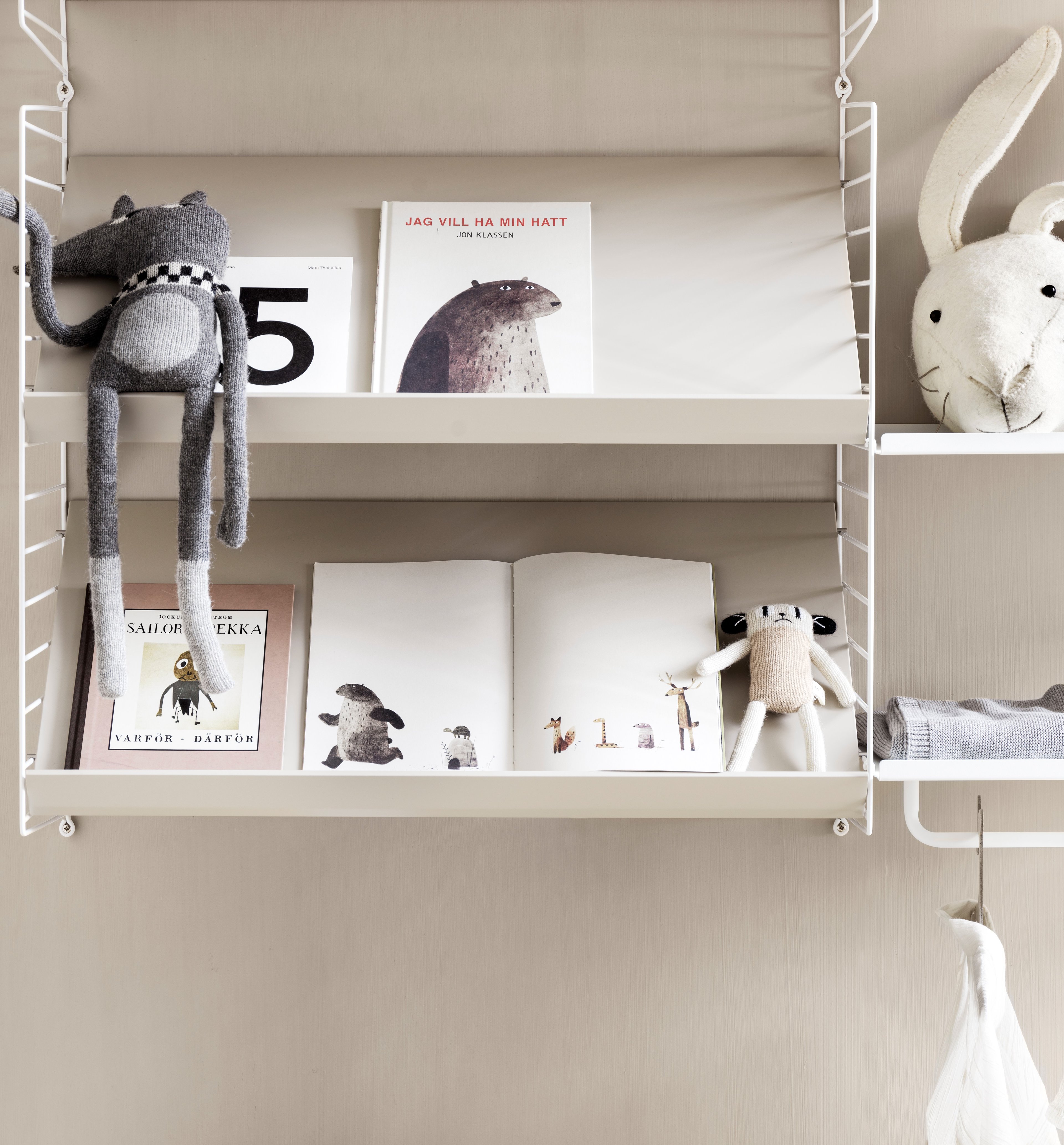 Wall mounted kids room solution from String. Wall panels, metal shelves low and rod in white. Magazine shelves solid in beige.