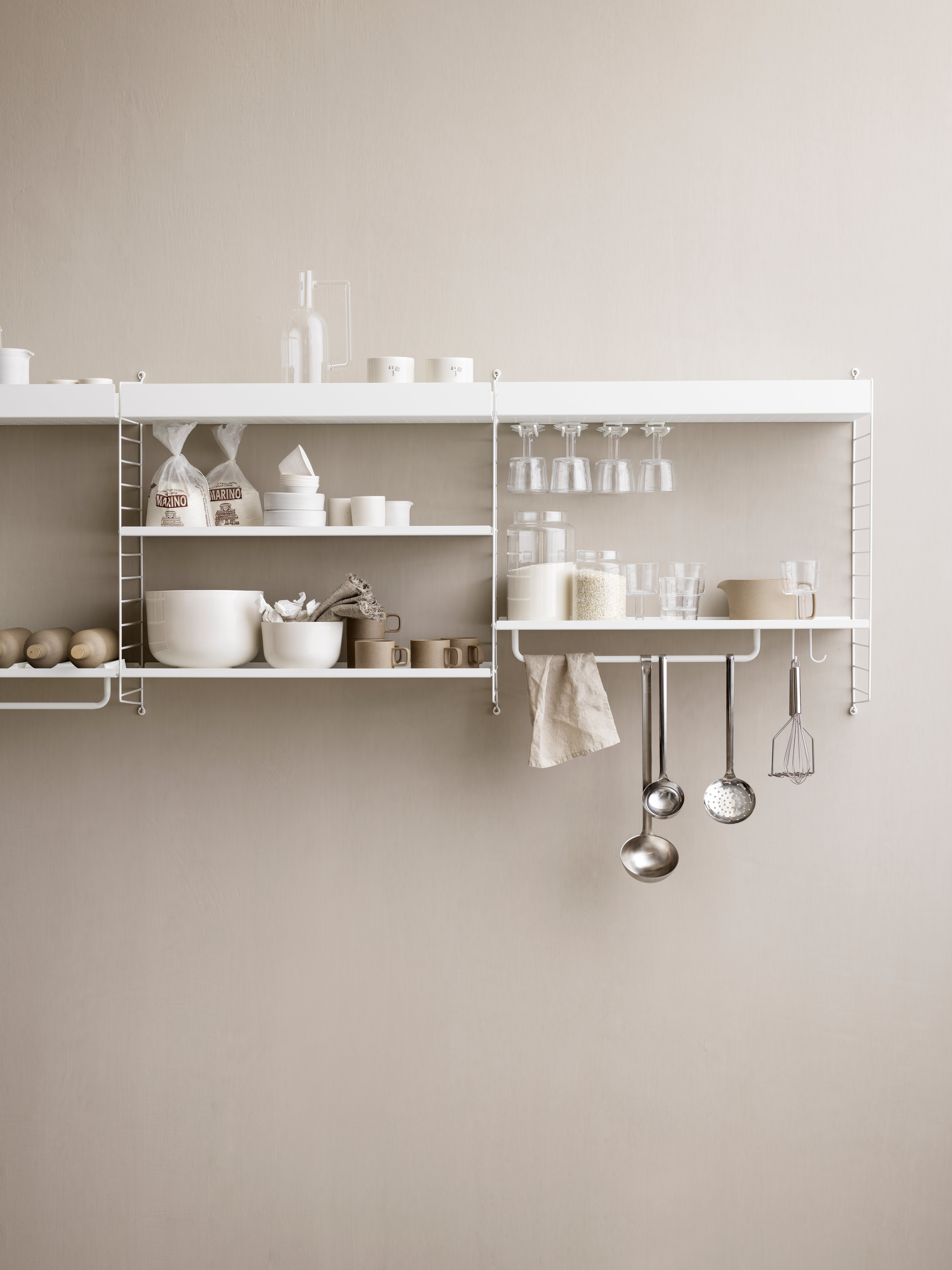 String shelving system for your kitchen. Wall panels in white, metal shelves with high and low edge in white, j hooks in white, hanger-racks in white and rods in white.