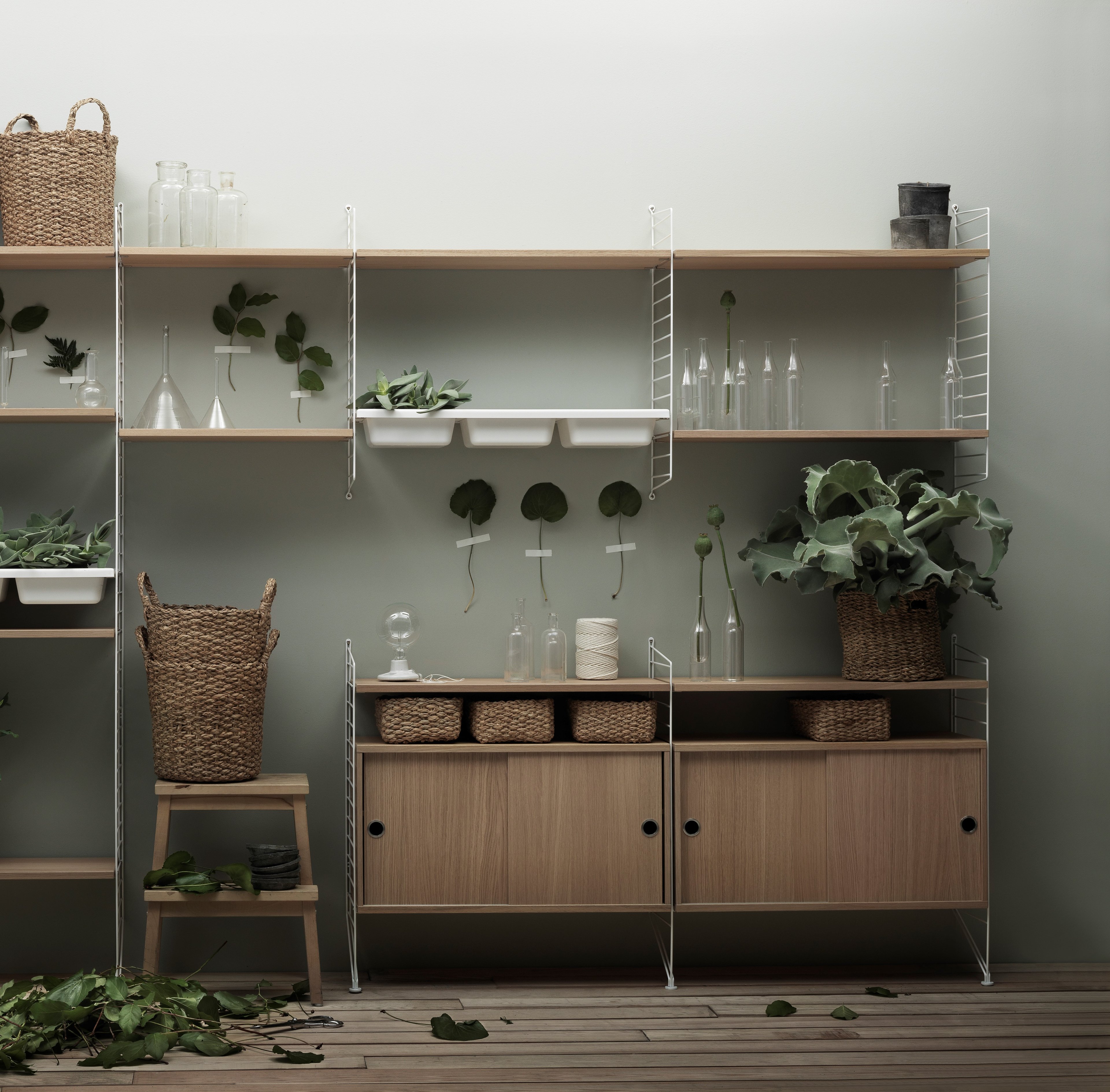 Floor mounted livingroom solution from String. Floor panels, wall panels and bowl shelf in white. Shelves and cabinets with sliding doors in oak.