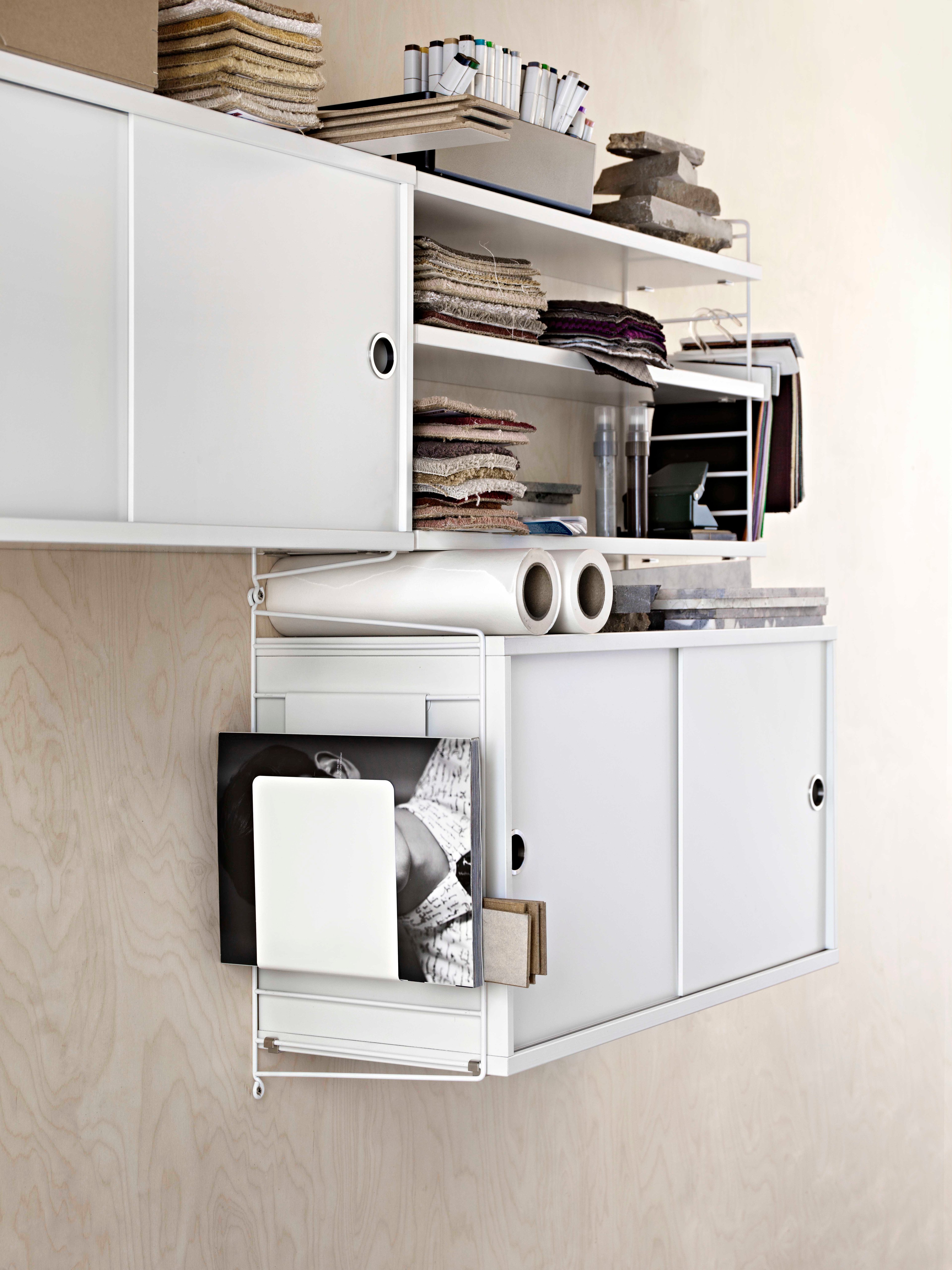 Wall mounted workspace solution from String. Wall panels, shelves and cabinet with sliding doors in white. Magazine holder in white.