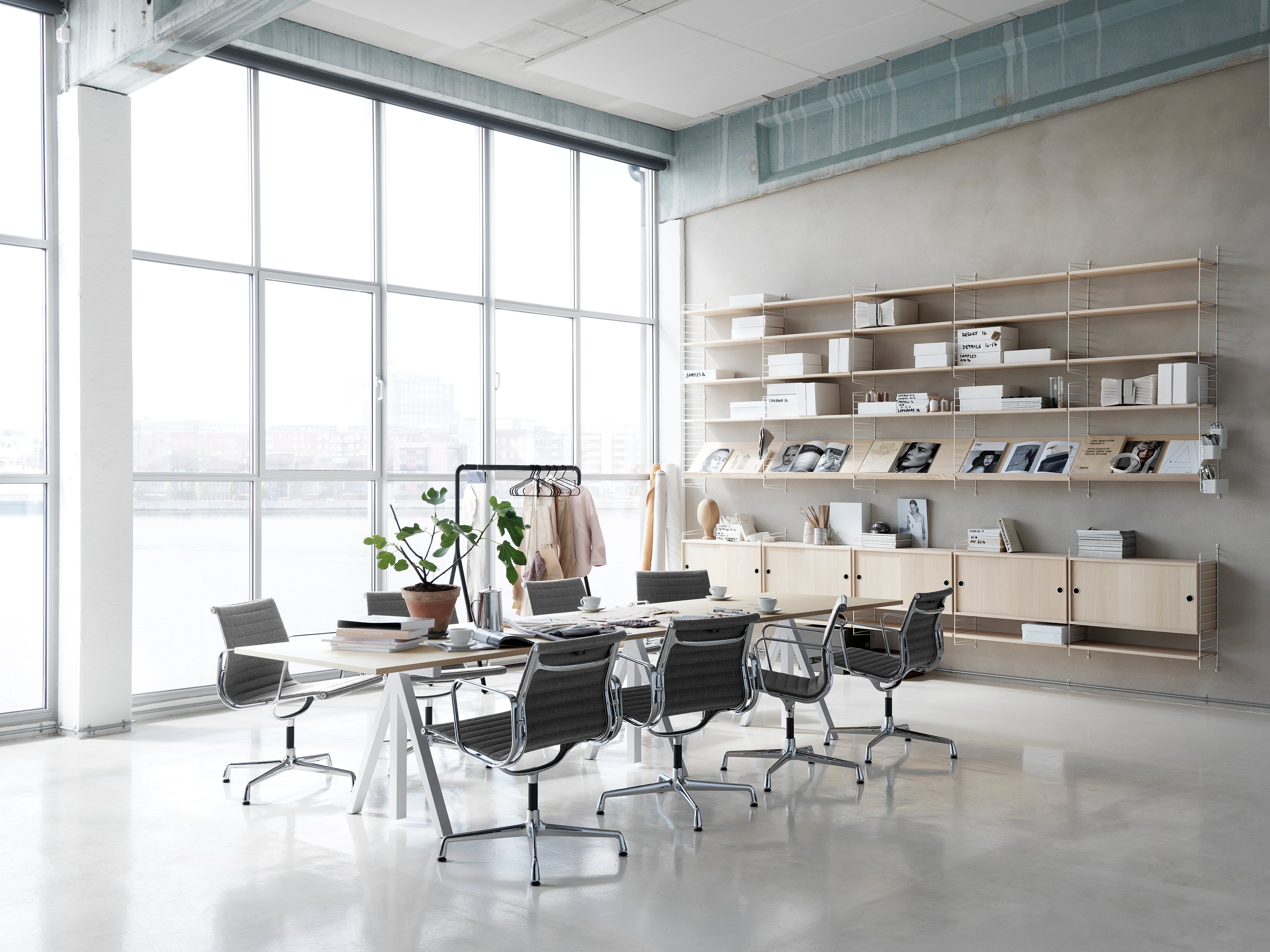 Wall mounted workspace solution from String. Height-adjustable conference table in ash. Wall panels in white. Shelves and cabinets with sliding doors in ash.